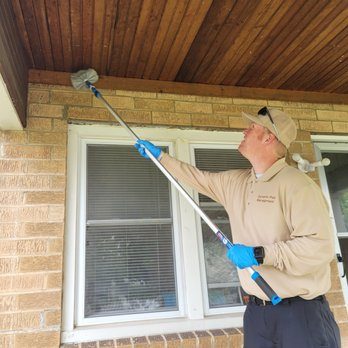 Brandon clearing spider webs from the eaves of a brick house